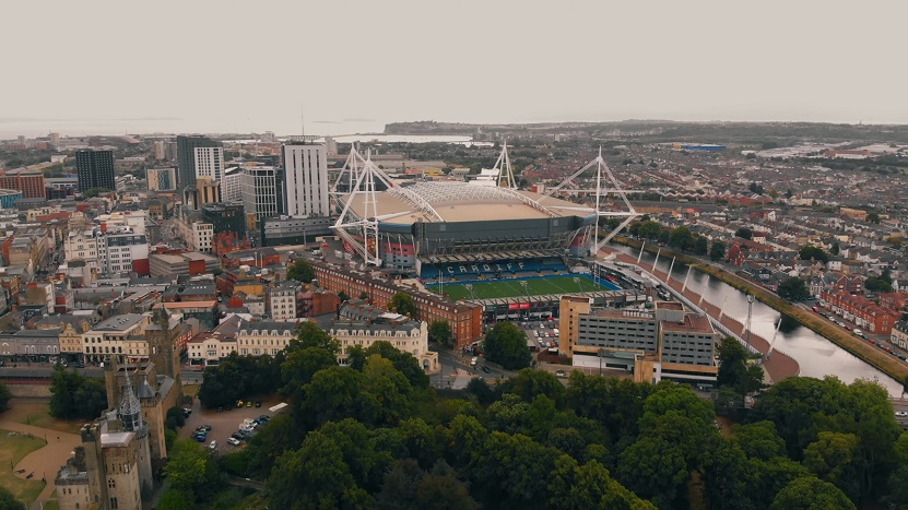 Aerial view of Cardiff featuring the Principality Stadium, surrounding urban landscape, riverbank housing, and city landmarks