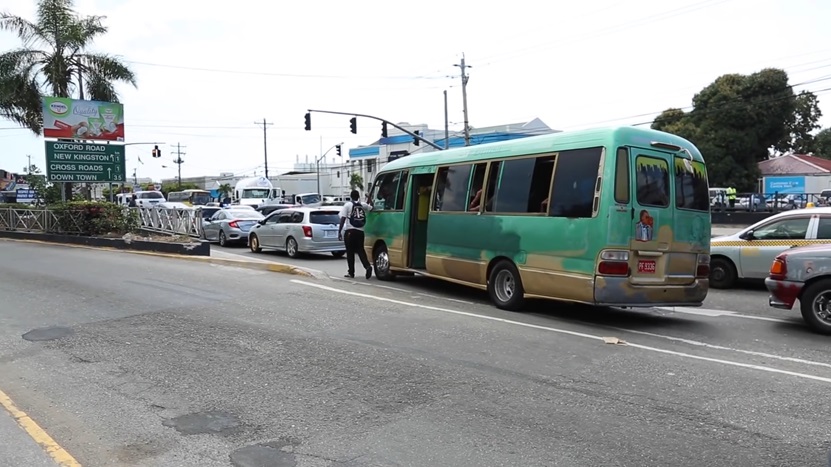 Jamaican traffic officer standing next to a green minibus during a routine stop on a busy road in Kingston