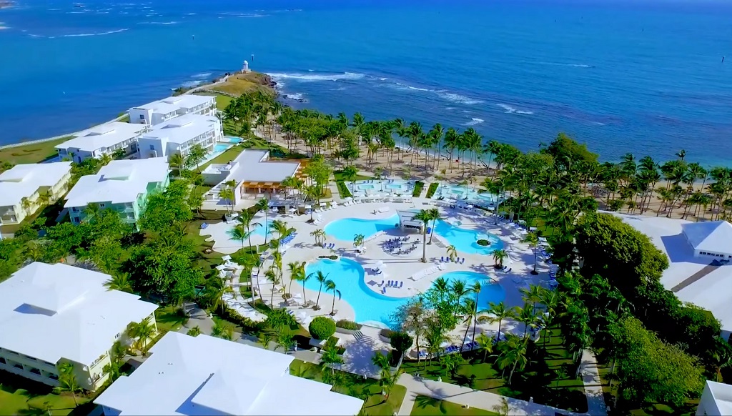 Aerial shot of a luxury beachfront resort with pools and palm trees.