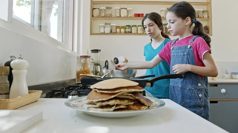 Two children making pancakes in the kitchen as a Mother's Day breakfast surprise