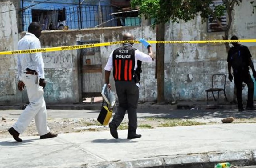 Jamaican police officers investigate a crime scene marked with yellow tape in a distressed urban area