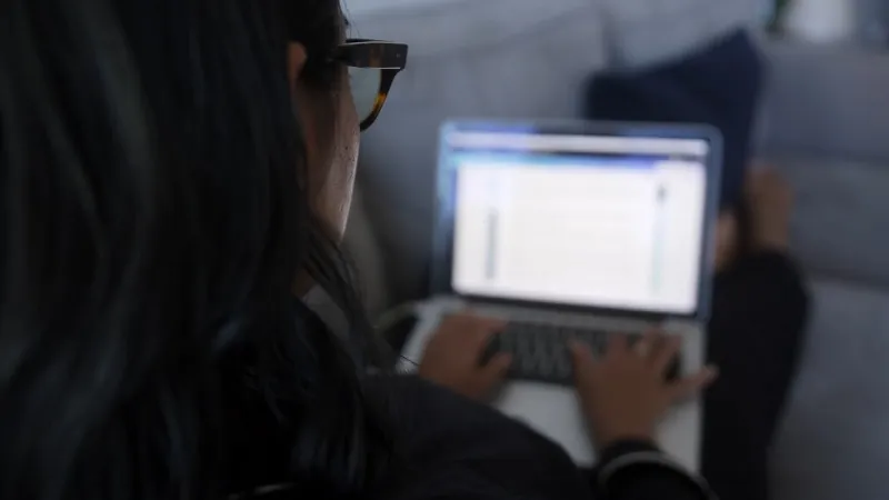 Woman wearing glasses working on a laptop while sitting on a couch