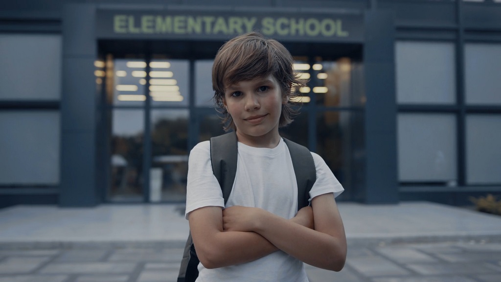 A young boy standing confidently in front of an elementary school building