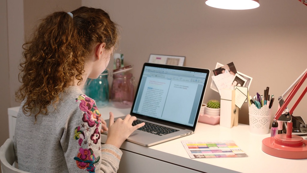 Young girl using a laptop for schoolwork in a modern, tech-friendly study space