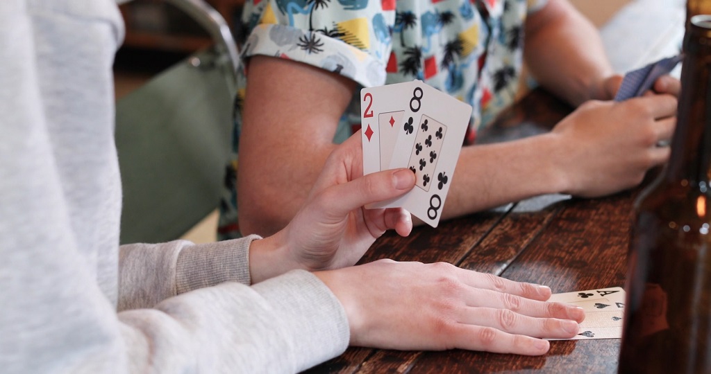 Close-up of adults playing poker with cards and drinks on the table, a classic pick among games for adults