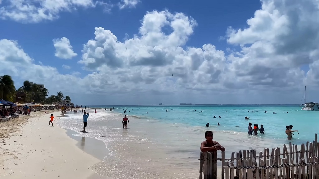 Tourists enjoying a sunny day at Playa Norte on Isla Mujeres near Cancun, with clear turquoise waters and palm-lined beach