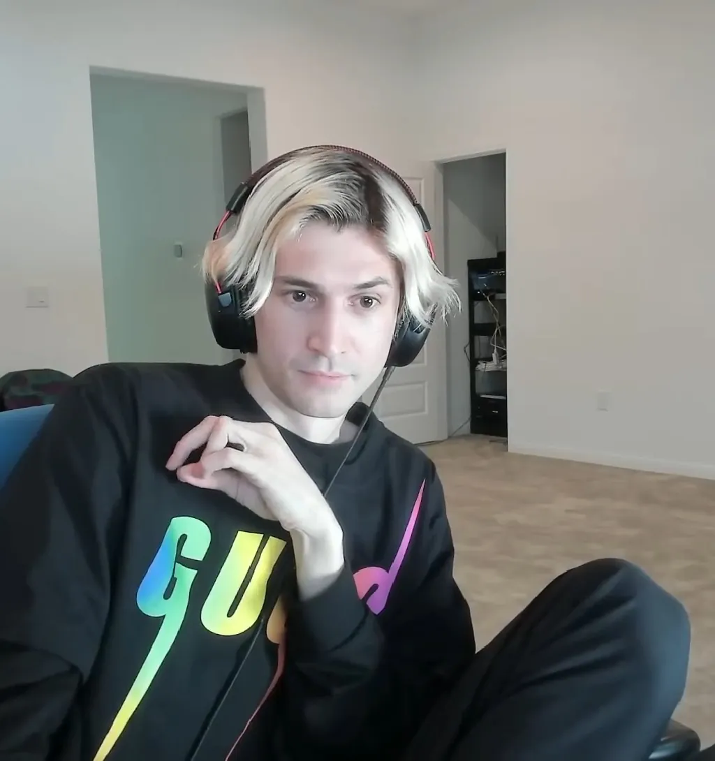 xQc speaking into a microphone during a podcast interview, wearing a black hoodie and headphones