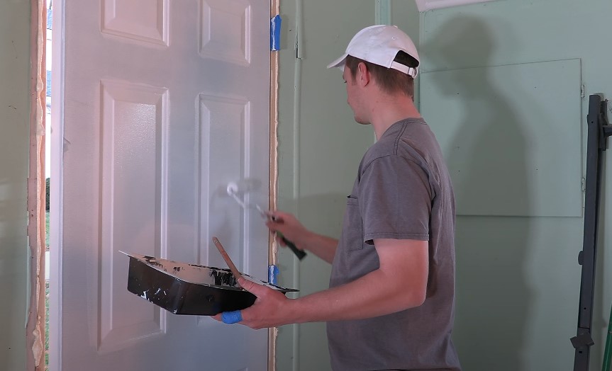A person applies paint to a door frame, focusing on precision