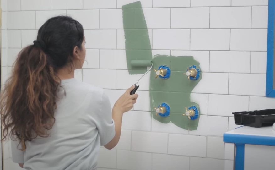 A person paints a section of a tiled wall