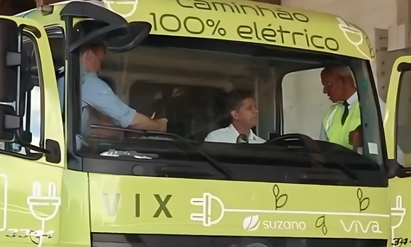 Two men sit inside a green truck inside a warehouse