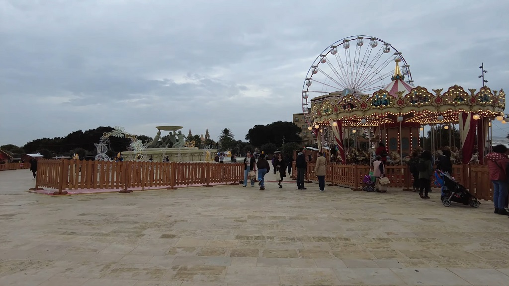 Triton Fountain Square in Valletta during Christmas, with a brightly lit carousel, Ferris wheel, and festive decorations