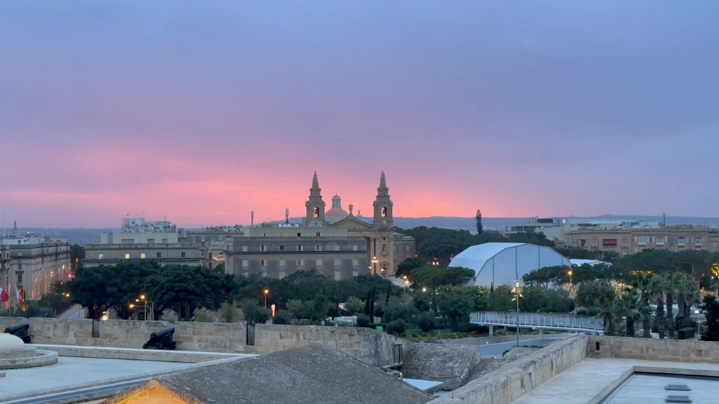 View of Valletta at sunset in December with pink and purple skies behind a historic church and surrounding buildings, illustrating Malta’s mild winter weather