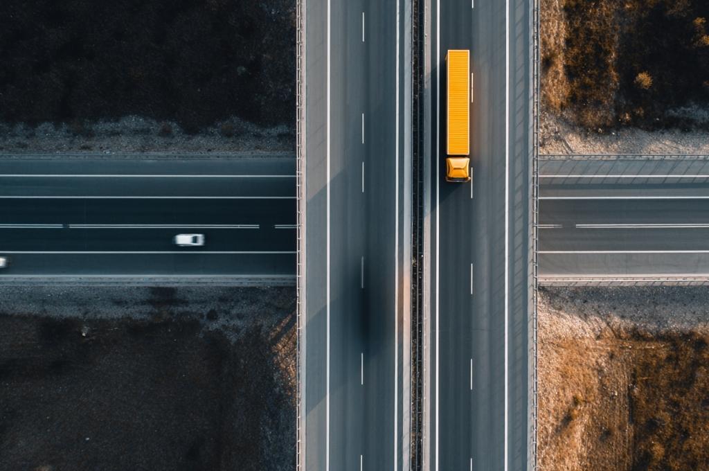 An aerial view of a highway with a yellow freight truck and passing vehicles