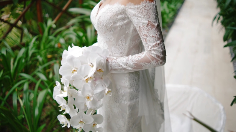 A bride in a detailed lace gown holds cascading white orchids that highlight textural couture elements