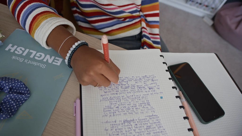 Student writing handwritten notes in a notebook during study time
