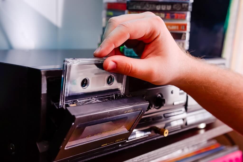 Hand inserting cassette tape into vintage audio player with stacked tapes in background