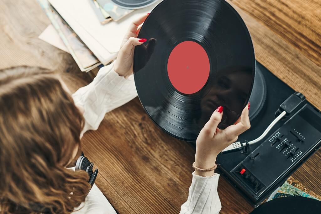 Person holding vinyl record above turntable in retro music setup