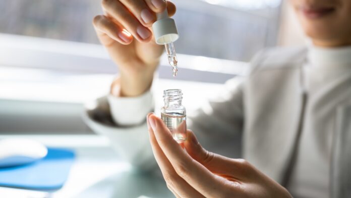 A person measures CBD oil with a dropper in a small glass bottle