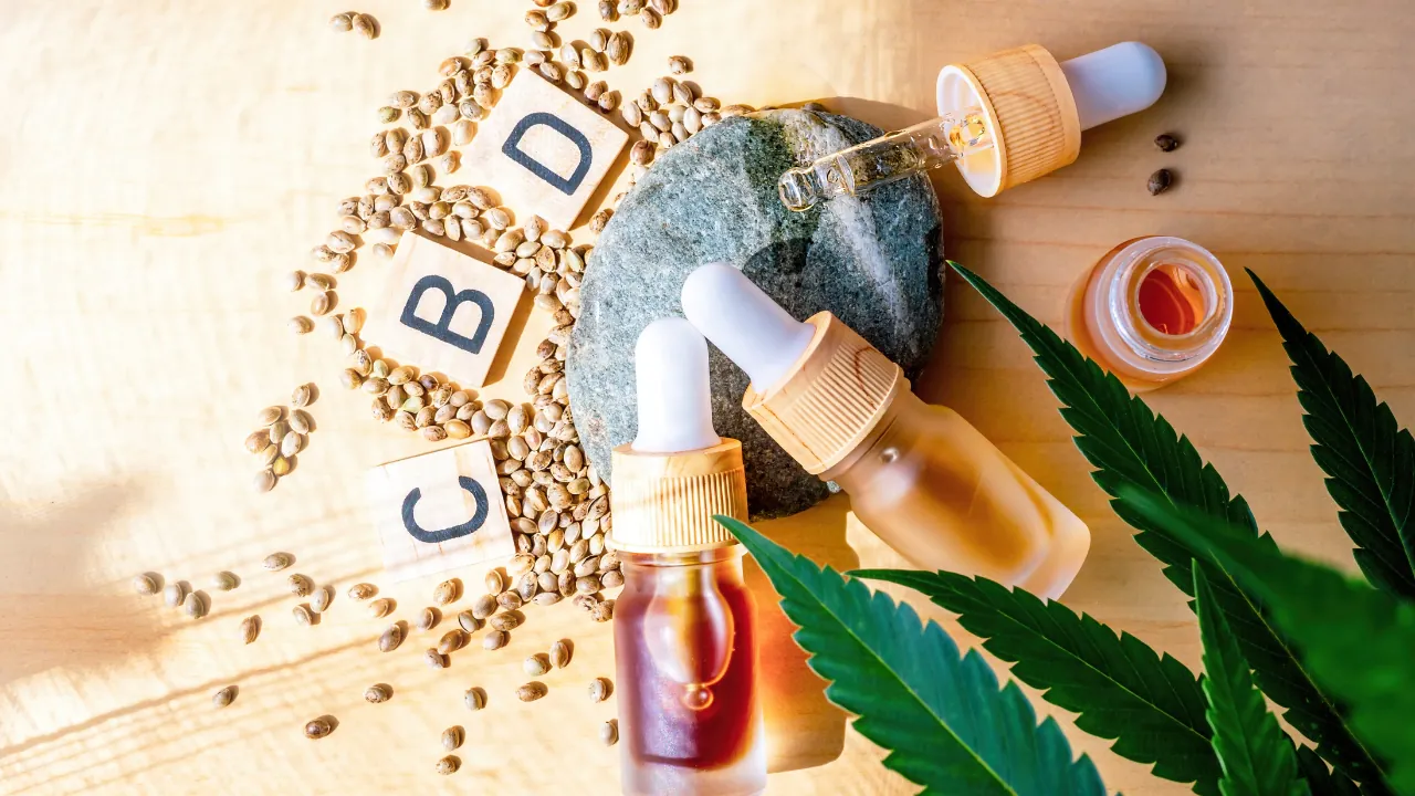 CBD oil bottles sit beside hemp seeds and cannabis leaves on a wooden surface