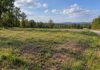 Buying Land to Build On? The Homework That Saves You Thousands Vacant buildable land parcel with grassy terrain, gravel road, trees, and nearby utility poles.